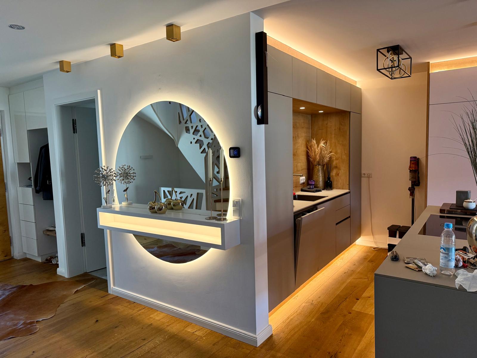 Modernisierter Eingangsbereich mit LED-beleuchtetem Rundspiegel und offener Designerküche